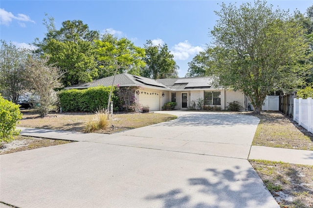 ranch-style house with driveway, roof mounted solar panels, stucco siding, an attached garage, and fence