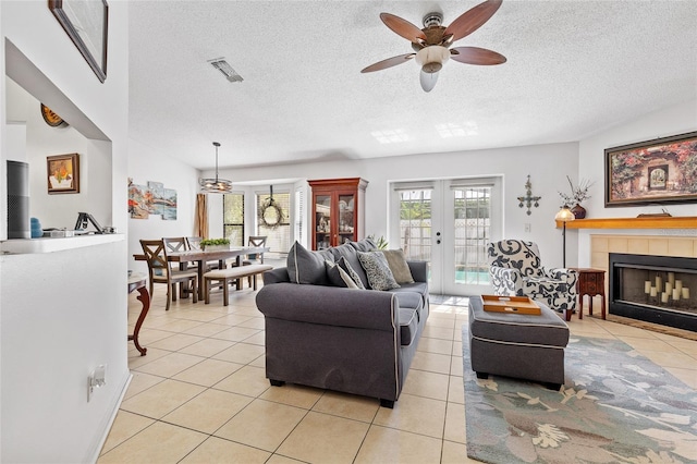 living room with a tile fireplace, light tile patterned flooring, a ceiling fan, visible vents, and french doors