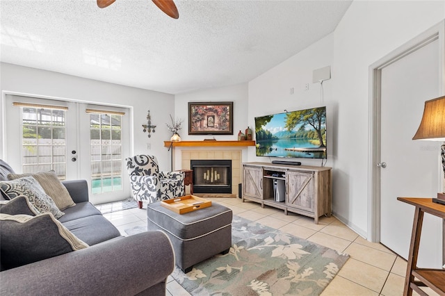 living area with a tile fireplace, light tile patterned floors, ceiling fan, a textured ceiling, and french doors