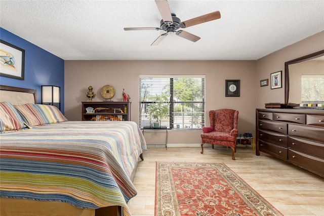 bedroom featuring a ceiling fan, a textured ceiling, multiple windows, and light wood-style flooring