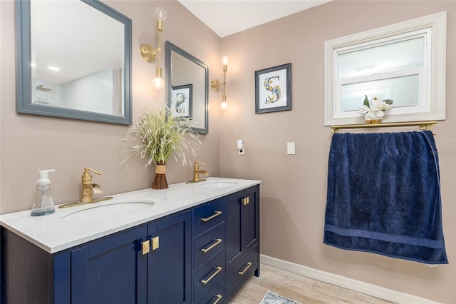 full bathroom with baseboards, wood finished floors, double vanity, and a sink