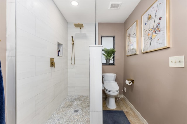 bathroom featuring visible vents, baseboards, toilet, wood finished floors, and tiled shower