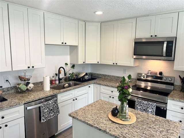 kitchen featuring a textured ceiling, appliances with stainless steel finishes, a sink, and white cabinets