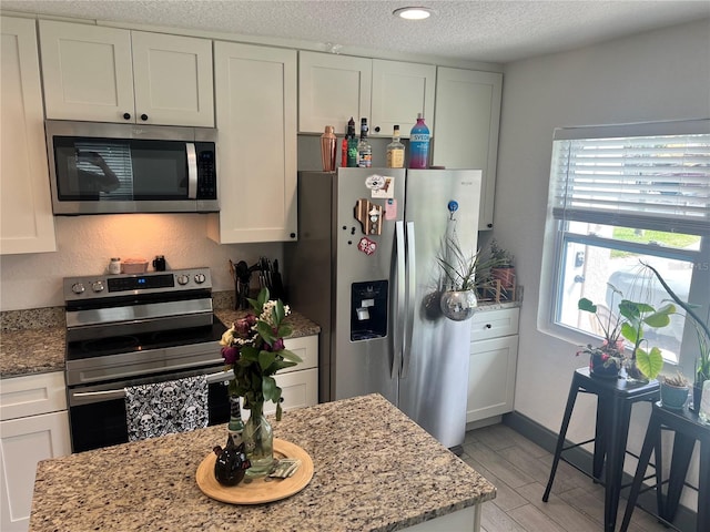 kitchen with a textured ceiling, appliances with stainless steel finishes, white cabinetry, and light stone countertops