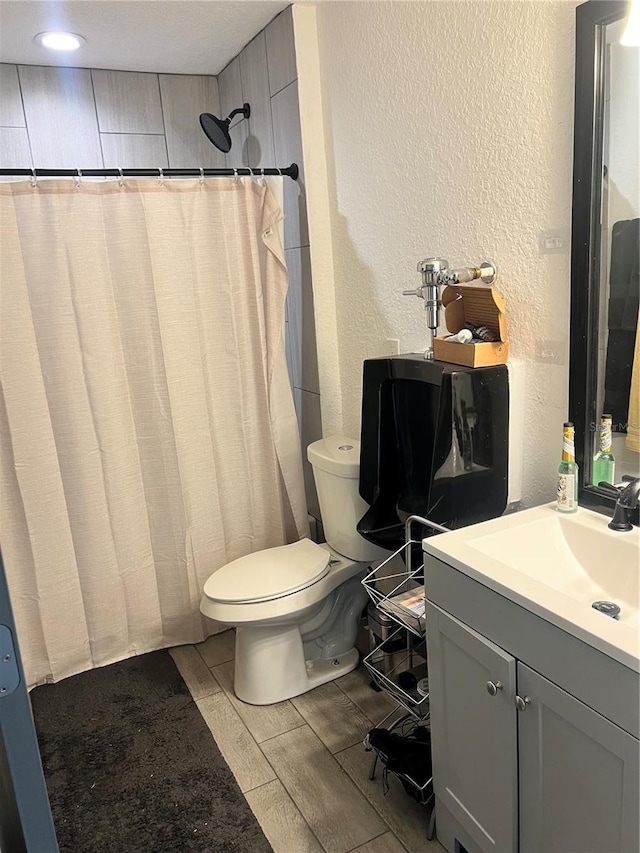 full bath featuring a shower with curtain, a textured wall, vanity, and toilet