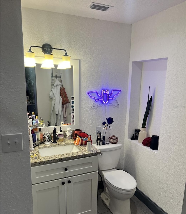 bathroom with visible vents, a textured wall, vanity, and toilet