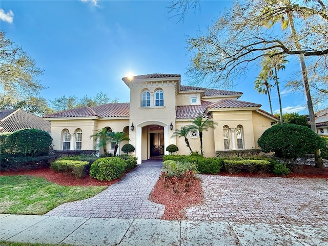 mediterranean / spanish-style home with decorative driveway, a tile roof, and stucco siding