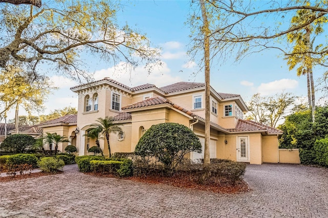 mediterranean / spanish-style home with decorative driveway, a tile roof, and stucco siding