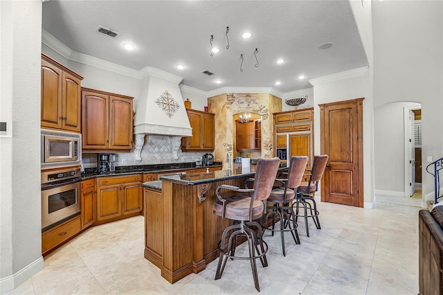 kitchen with arched walkways, stainless steel appliances, a breakfast bar, custom exhaust hood, and a center island with sink