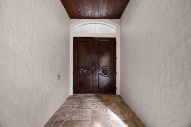 doorway featuring a textured wall, wood ceiling, and stone tile floors