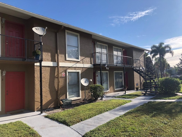 view of front of property with a front yard, stucco siding, a balcony, and stairs