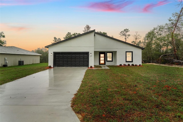 view of front of property with central AC unit, an attached garage, concrete driveway, a yard, and stucco siding