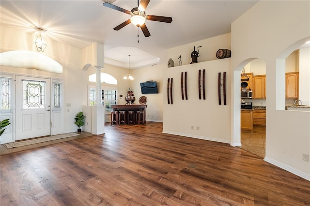 foyer featuring a raised ceiling, a ceiling fan, arched walkways, baseboards, and dark wood-style flooring