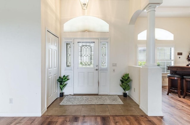 entrance foyer with wood finished floors, baseboards, a high ceiling, decorative columns, and arched walkways