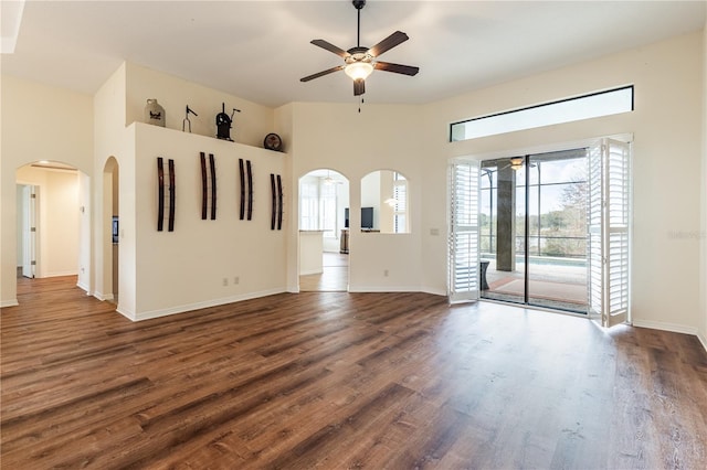 unfurnished living room featuring baseboards, arched walkways, dark wood-type flooring, and a ceiling fan