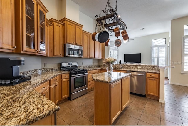 kitchen with light tile patterned floors, brown cabinets, appliances with stainless steel finishes, and a peninsula