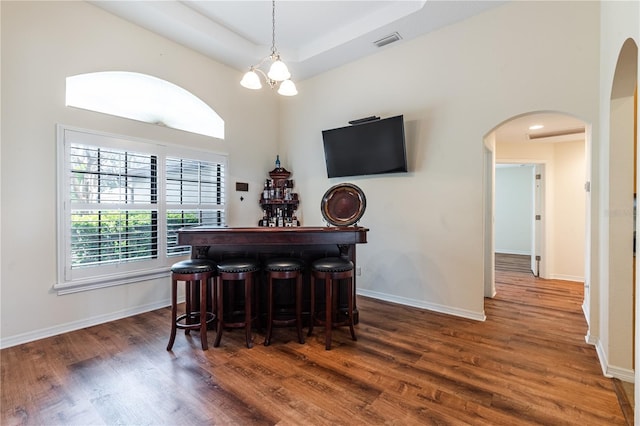 dining area featuring arched walkways, a bar, baseboards, and wood finished floors