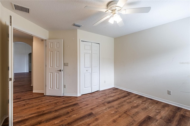 unfurnished bedroom featuring visible vents, arched walkways, a closet, and wood finished floors