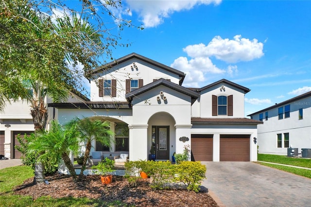 mediterranean / spanish-style house featuring a garage, central AC unit, covered porch, decorative driveway, and stucco siding