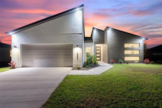 modern home with an attached garage, driveway, a lawn, and stucco siding