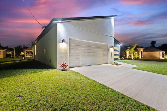 property exterior at dusk featuring driveway, a lawn, an attached garage, and stucco siding