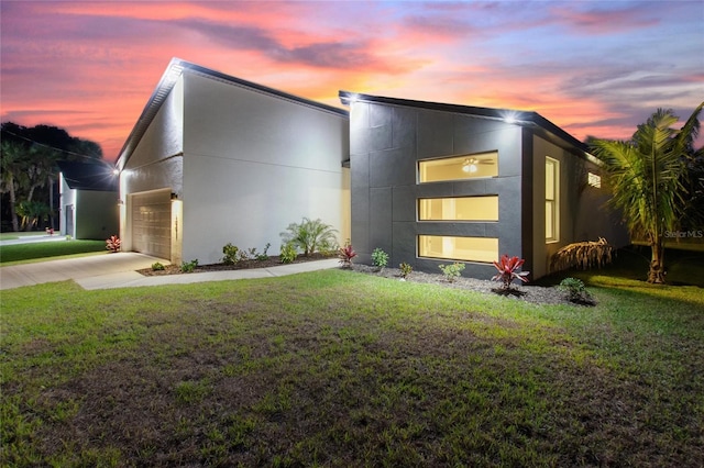 contemporary home featuring a garage, concrete driveway, a lawn, and stucco siding