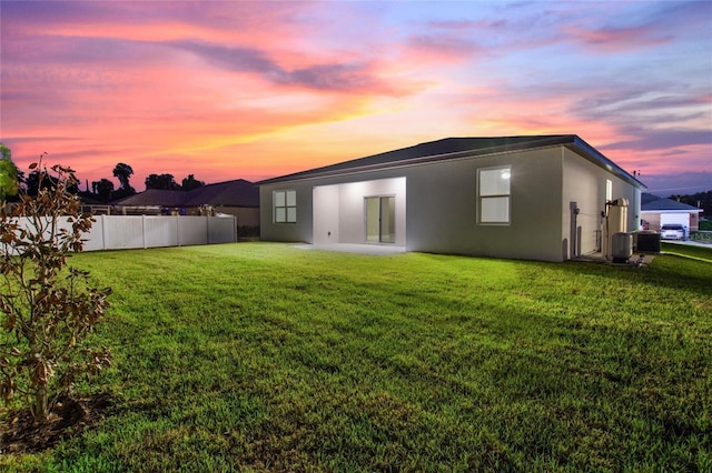 back of property at dusk featuring a yard, central AC, fence, and stucco siding