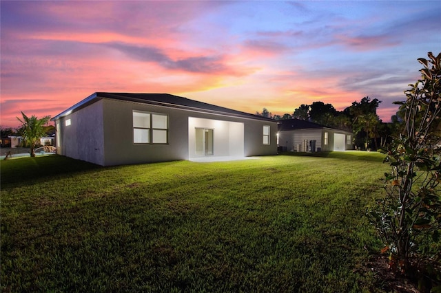 rear view of property featuring a lawn, a patio area, and stucco siding