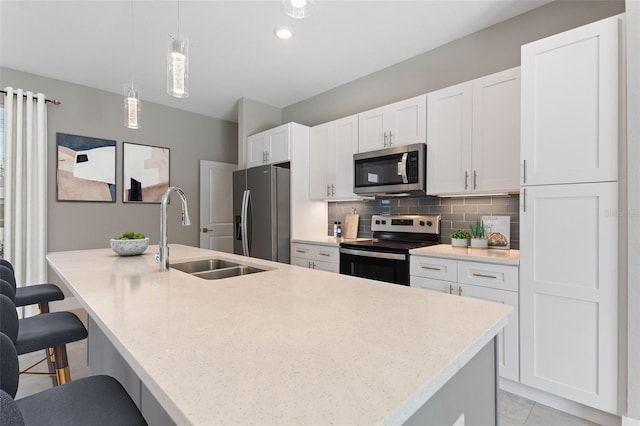 kitchen with appliances with stainless steel finishes, a kitchen breakfast bar, light countertops, pendant lighting, and a sink