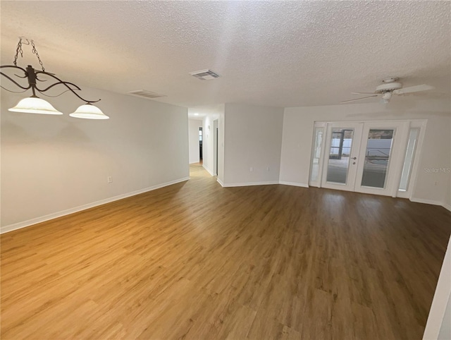 spare room with a textured ceiling, wood finished floors, visible vents, baseboards, and french doors