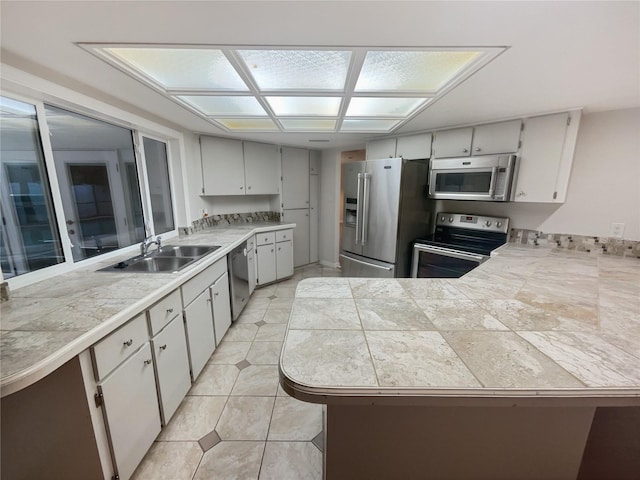 kitchen with light tile patterned floors, stainless steel appliances, white cabinetry, a sink, and a peninsula