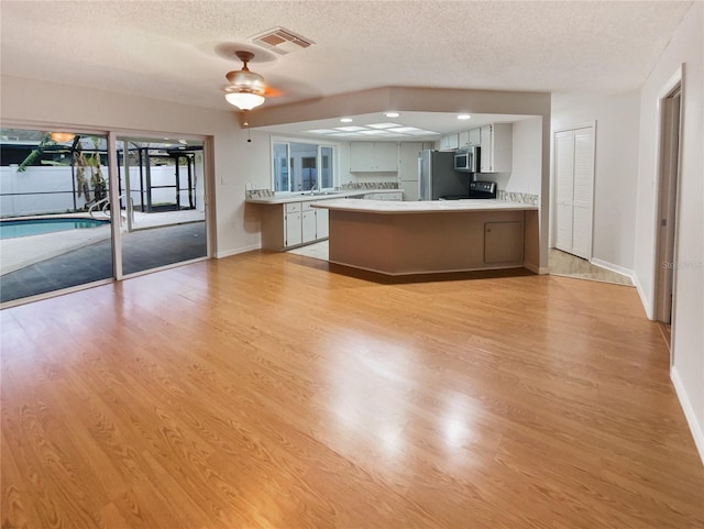 kitchen with a peninsula, stainless steel appliances, visible vents, light countertops, and light wood-type flooring