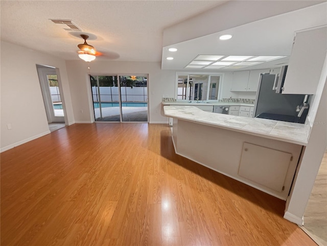 kitchen featuring visible vents, freestanding refrigerator, a peninsula, light countertops, and white cabinetry