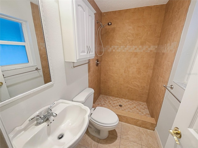 bathroom with tiled shower, a sink, toilet, and tile patterned floors