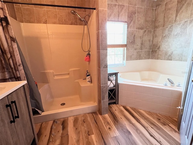 bathroom with a stall shower, tiled tub, wood finished floors, and vanity