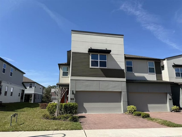 contemporary home with an attached garage, a front yard, decorative driveway, and stucco siding