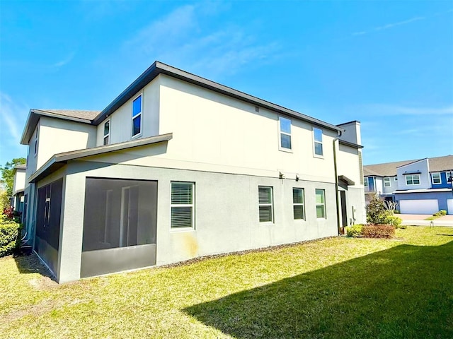 back of house with stucco siding, a sunroom, and a yard