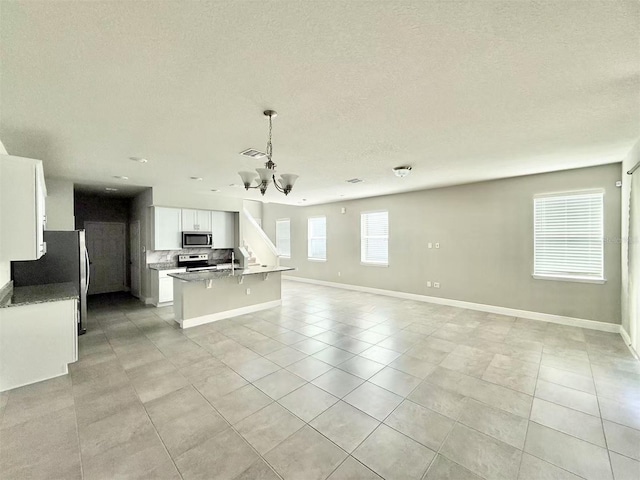 kitchen featuring a center island with sink, open floor plan, stainless steel appliances, white cabinetry, and a notable chandelier