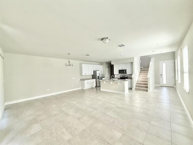 unfurnished living room with visible vents, an inviting chandelier, a sink, baseboards, and stairs