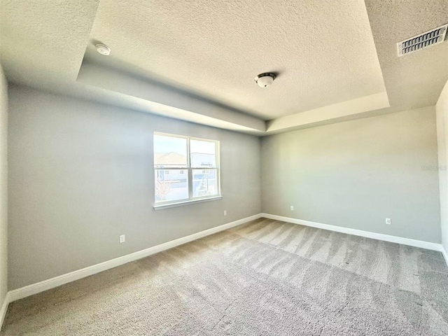 carpeted empty room featuring baseboards, a textured ceiling, visible vents, and a tray ceiling