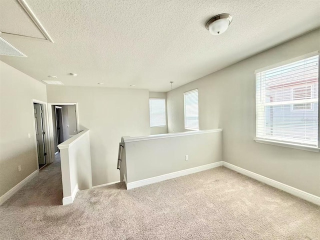 empty room with a textured ceiling, carpet floors, visible vents, and baseboards