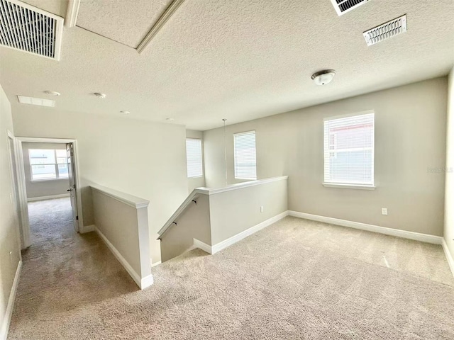 carpeted empty room with baseboards, visible vents, and a textured ceiling