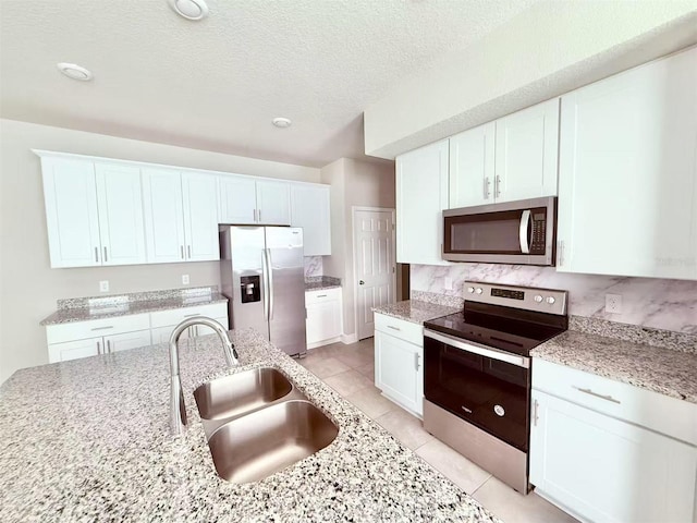 kitchen featuring appliances with stainless steel finishes, white cabinets, a sink, and light stone counters