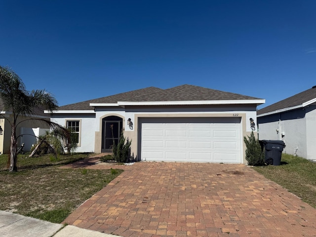 single story home with decorative driveway, roof with shingles, an attached garage, and stucco siding