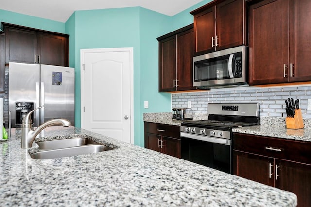 kitchen with light stone countertops, tasteful backsplash, appliances with stainless steel finishes, and a sink