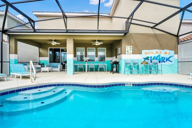 view of swimming pool featuring glass enclosure, a patio area, outdoor dry bar, and a ceiling fan