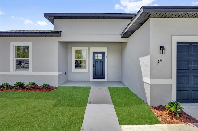 view of exterior entry with a lawn, a garage, and stucco siding