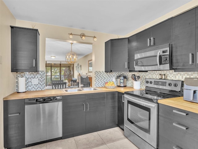 kitchen featuring light tile patterned floors, a sink, decorative backsplash, appliances with stainless steel finishes, and butcher block counters