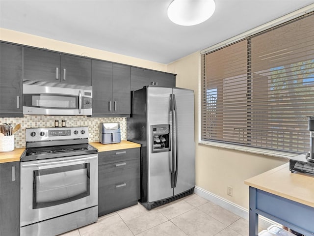 kitchen with light tile patterned floors, tasteful backsplash, appliances with stainless steel finishes, and wood counters