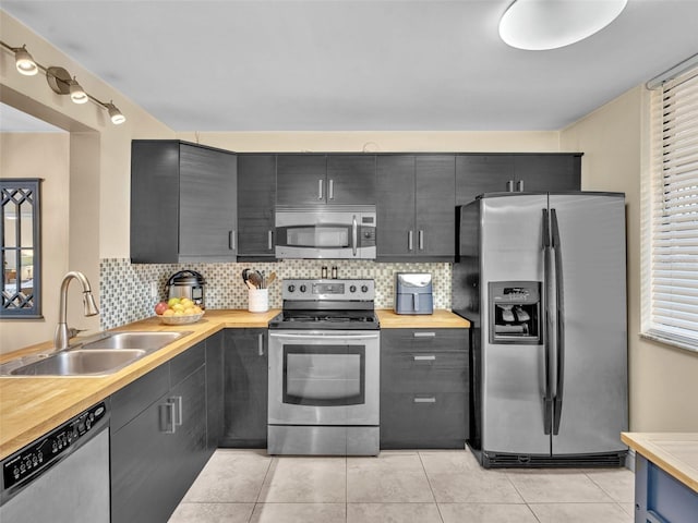 kitchen featuring light tile patterned floors, decorative backsplash, appliances with stainless steel finishes, dark cabinetry, and a sink